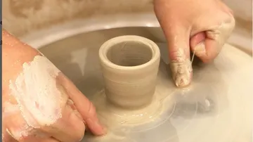 Hands shaping pottery on spinning wheel.