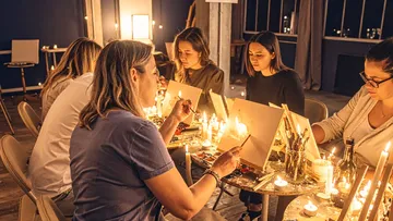 Frauen malen bei Kerzenlicht drinnen.