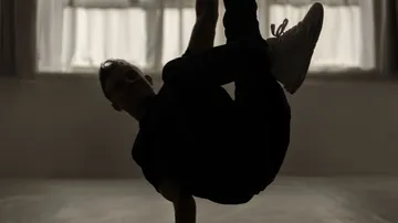 Person breakdancing indoors with curtains.