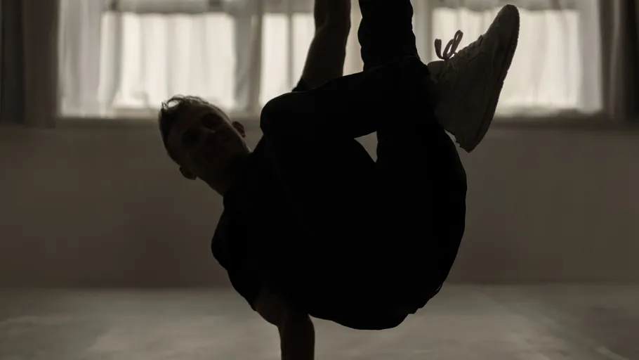 Person breakdancing indoors with curtains.