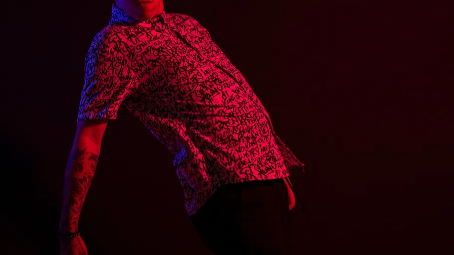 Person leaning in patterned shirt, dark background.