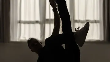 Silhouette of dancer stretching in dimly lit room.