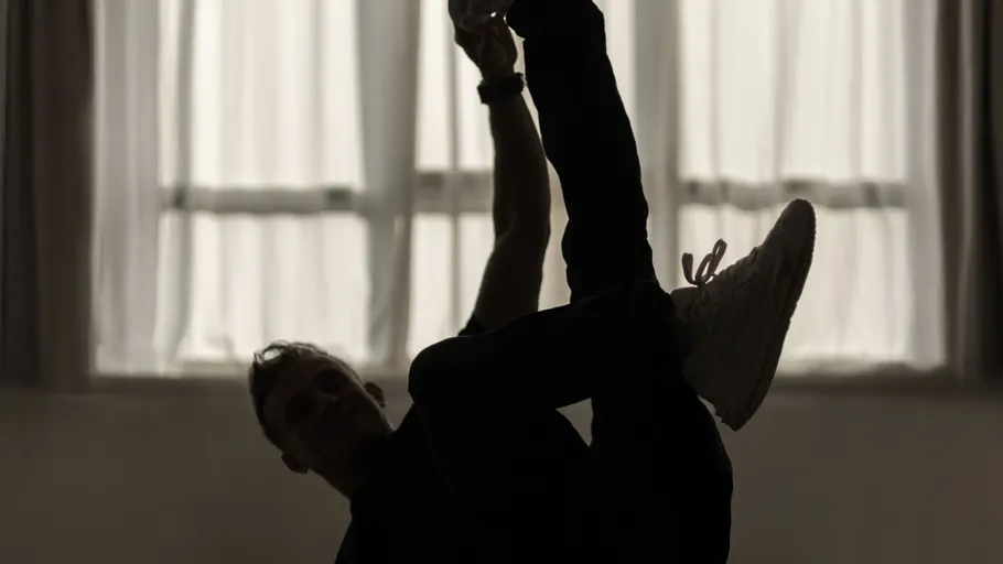Silhouette of dancer stretching in dimly lit room.