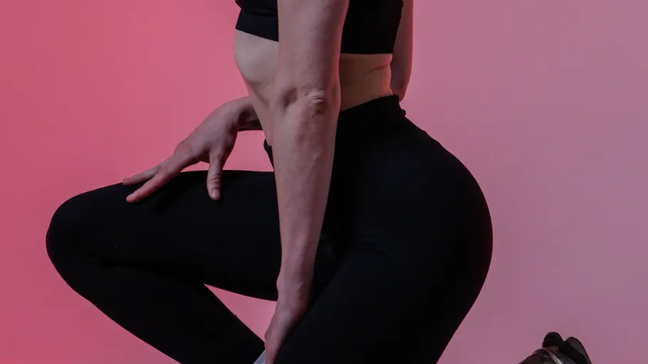 Person kneeling, wearing athletic wear, pink background.