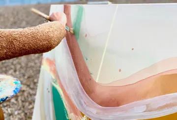 Person painting abstract art on large canvas outdoors.