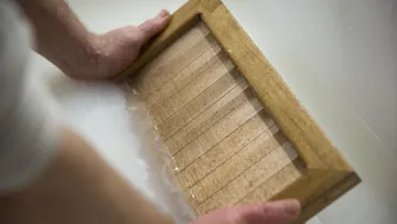 Hände halten Holzrahmen im Wasser.
