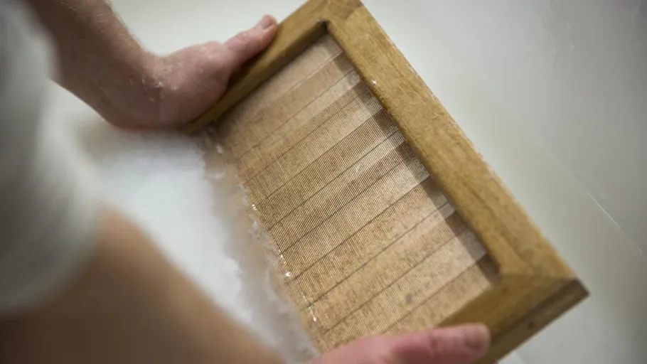 Hands holding wooden frame in water.