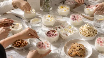 Hände dekorieren Desserts mit Blumen auf Tisch.