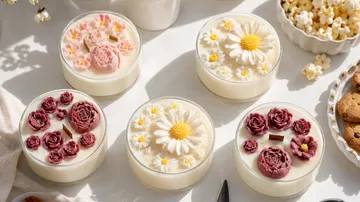 Vier floral dekorierte Kerzen auf Tisch.