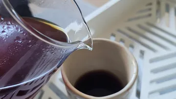Glaskanne gießt Kaffee in Keramikbecher.