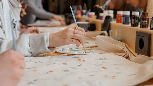 Person painting tote bag at table.