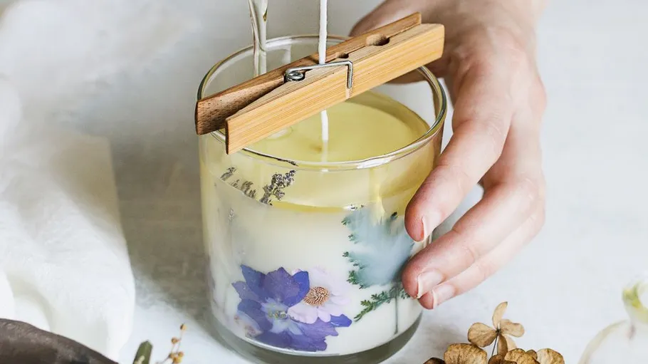 Hand holding candle with floral decorations.