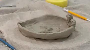 Clay bowl on fabric with tools around.