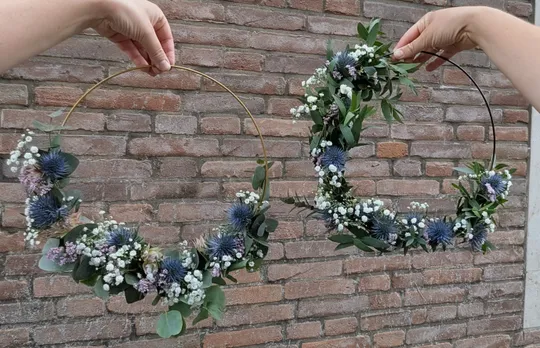 Hands holding floral wreaths against brick wall.