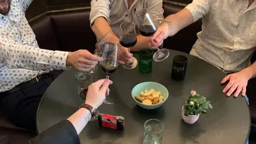 Vier Personen stoßen mit Weingläsern an einem Tisch an.