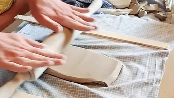 Hands rolling clay with a pin indoors.