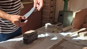 Person stacking clay pieces on a table.