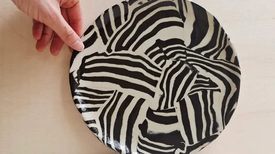 Hand holding striped plate on table.