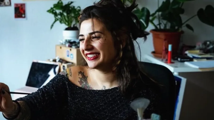 Woman smiling, sitting in a plant-filled room.