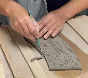 Hände schnitzen Ton mit grünem Werkzeug, Tischoberfläche.