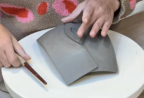 Hands sculpting clay on a round table.