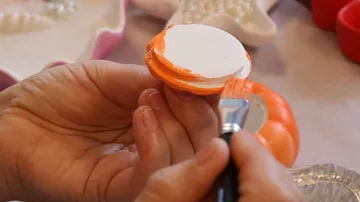 Hände bemalen kleines rundes Objekt orange.