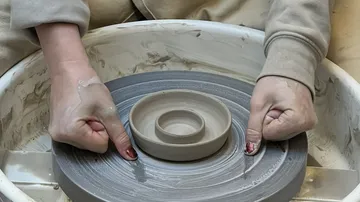 Hands shaping clay on a pottery wheel.