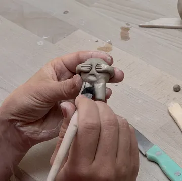 Hände modellieren kleine Tonfigur auf Tisch.