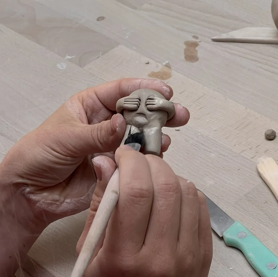 Hands sculpting small clay figure on table.