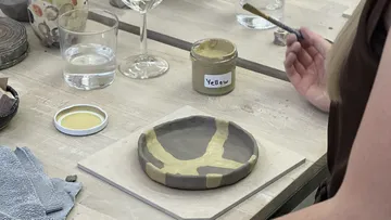 Person painting pottery on wooden table.