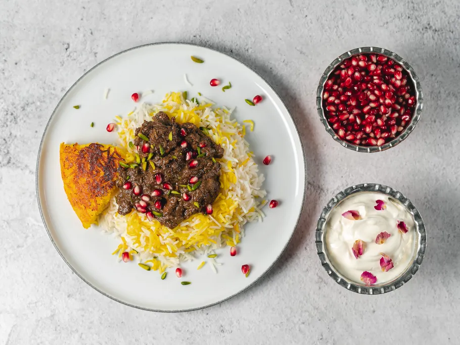 Ein Teller mit Reis, Fleisch, Granatapfelkernen und Joghurt.