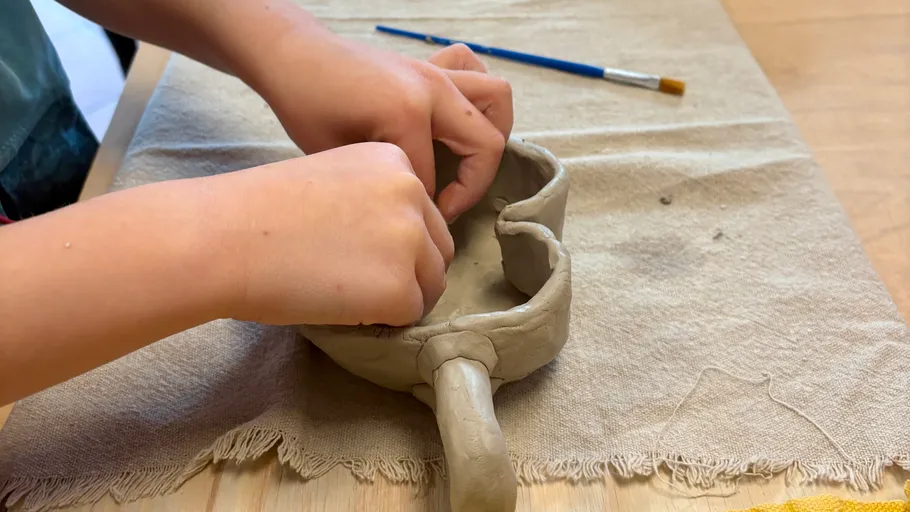 Child sculpting clay mug on table.