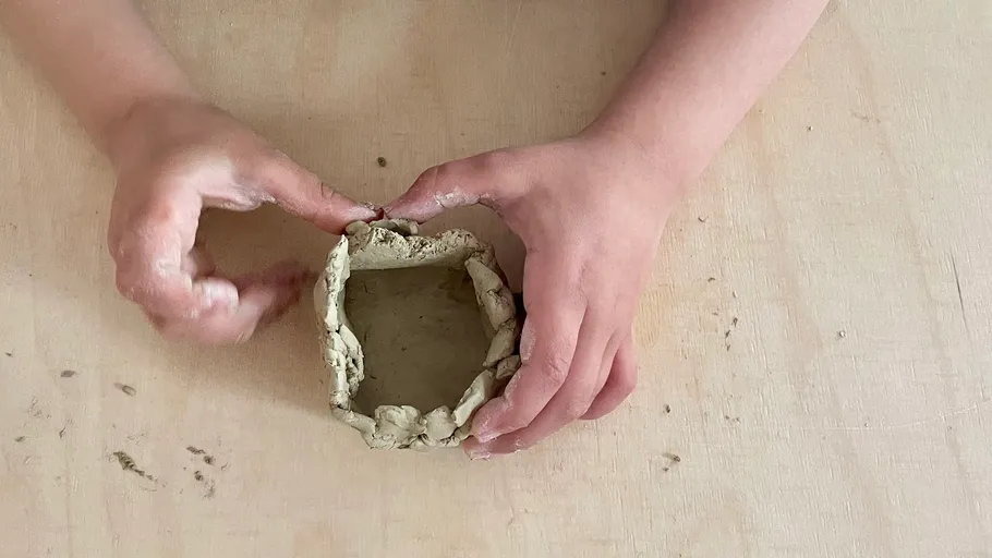 Hands shaping clay pot on wooden table.