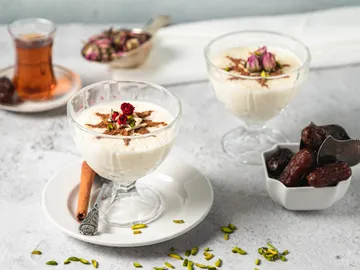Two dessert bowls with rice pudding and rose petals, and dates next to them.