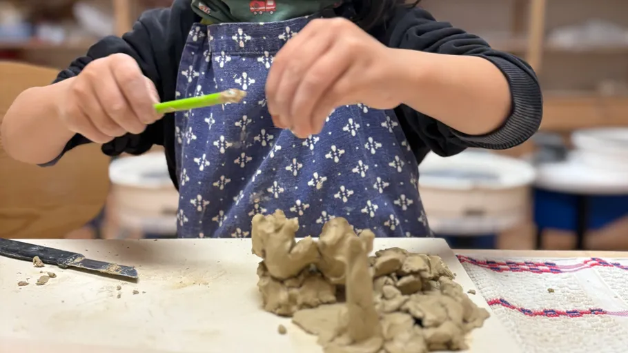 Child shaping clay with a tool indoors.