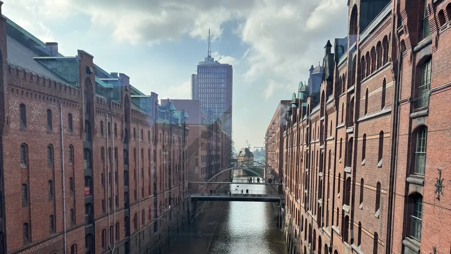 Brick buildings flank canal under bridge.