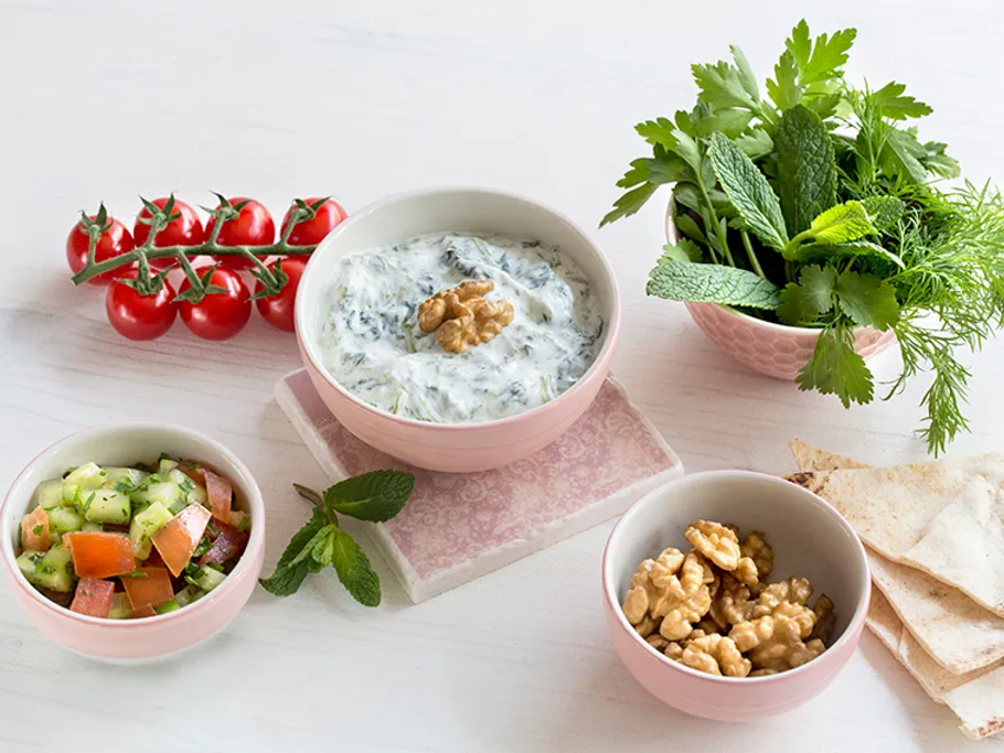 Dips, salad and fresh herbs arranged on a table.