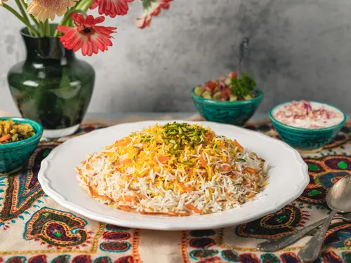 Colourful rice on a plate surrounded by side dishes.