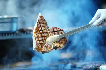 Steak mit Zange gegriffen auf Grill.