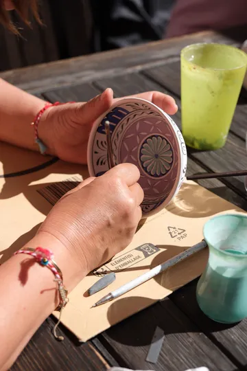 Hands painting a decorative bowl outdoors.