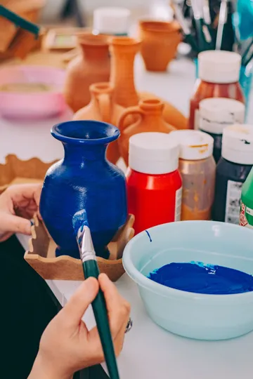 Hand bemalt blaue Vase, umgeben von Farben.
