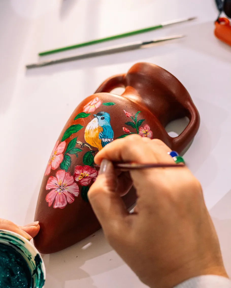 Person paints bird on pottery vase.