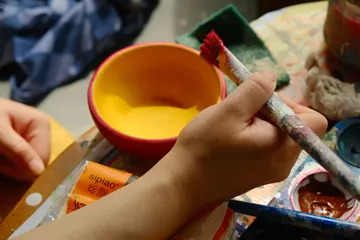 Hand hält Pinsel nahe roter Schüssel.