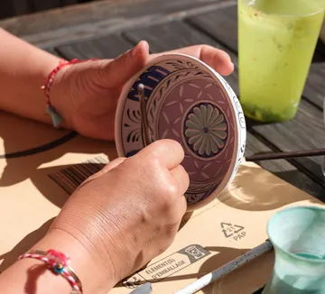 Hands painting a round ceramic object outdoors.