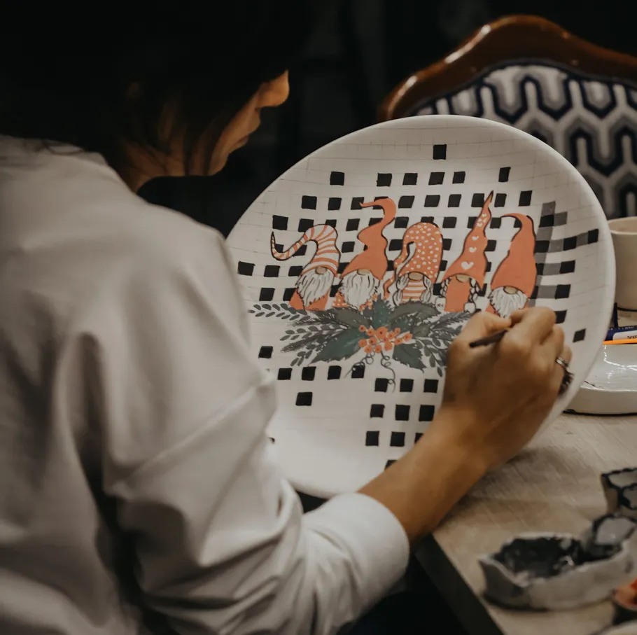 Person painting gnomes on a ceramic plate.