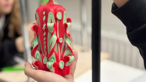 Hand hält kunstvoll geschnitzte rote Kerze drinnen.