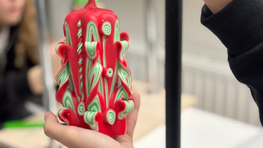 Hand holds intricately carved red candle indoors.