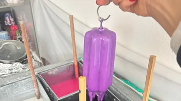 Purple candle being dipped, hand holding.