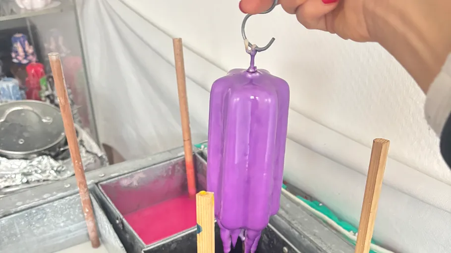 Purple candle being dipped, hand holding.
