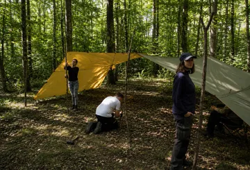 People setting up tarps in a forest.